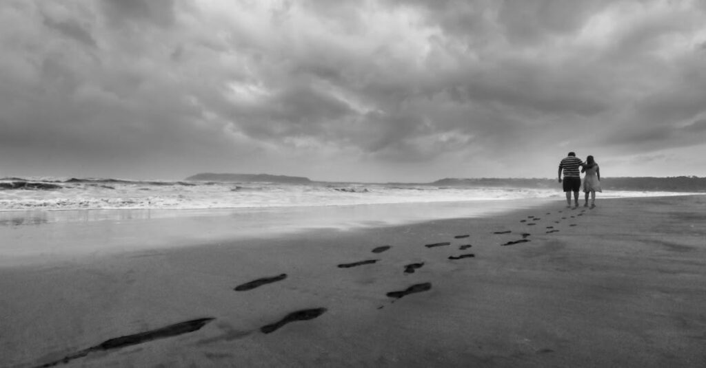 Grayscale Photo of Couple Walking on Seashore